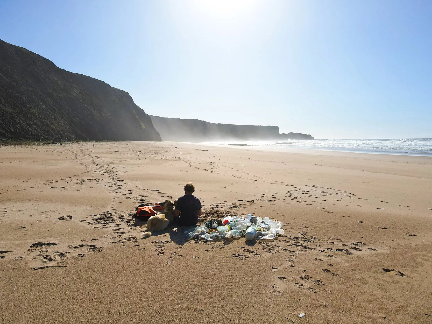 Ben with his dog sat in a beautiful beach in Portugal. Next to him is a pile of plastic he cleared from the beach.